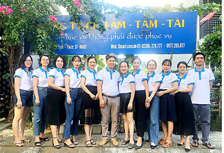 Tập thể nhân viên Tâm - Tầm - Tài trước biển hiệu công ty
